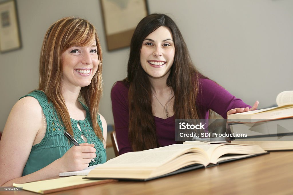 Due sorridente donna studenti universitari che studiano in libreria - Foto stock royalty-free di Adulto
