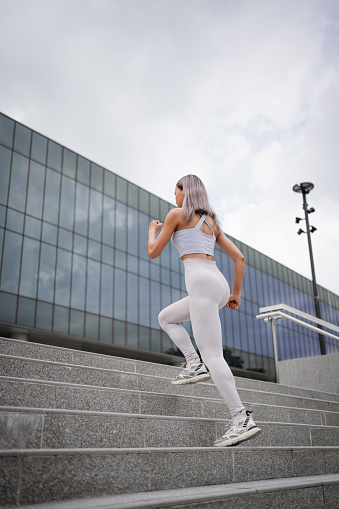 Young woman in sports attire is running on the city stairs.