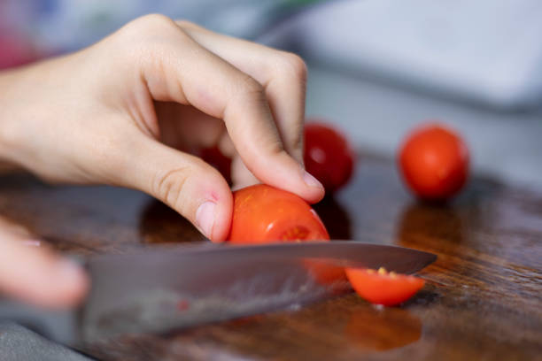 child's hand cuts a cherry tomato on a cutting board