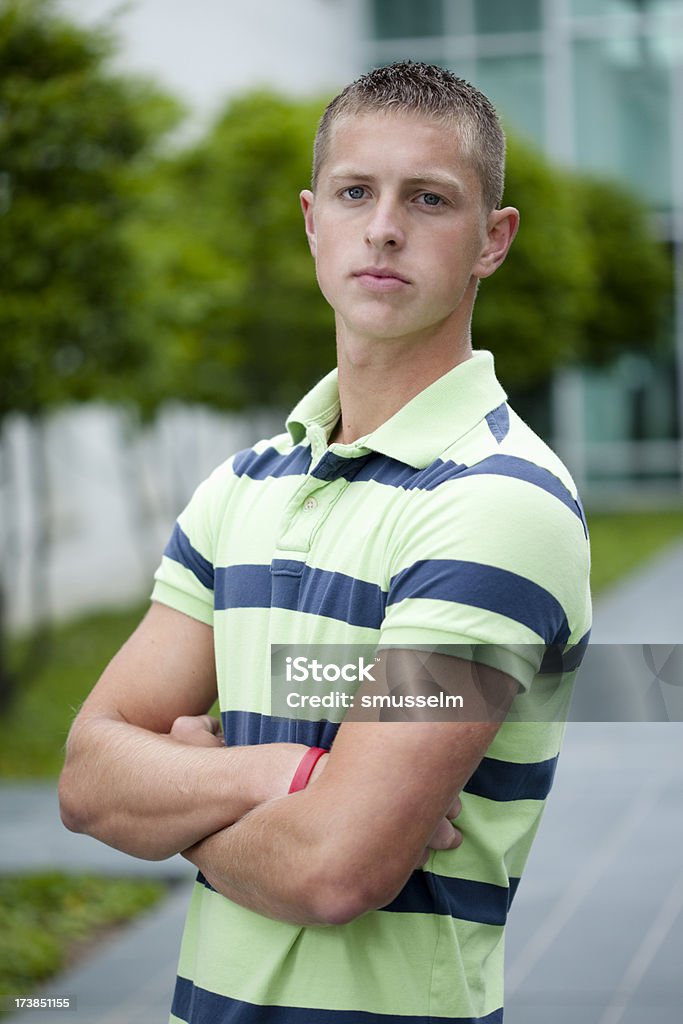 Headshot of a young man Graduating high school senior/college freshman crossing his arms in front of trees. Building in the background can look like university building. Blue Eyes Stock Photo