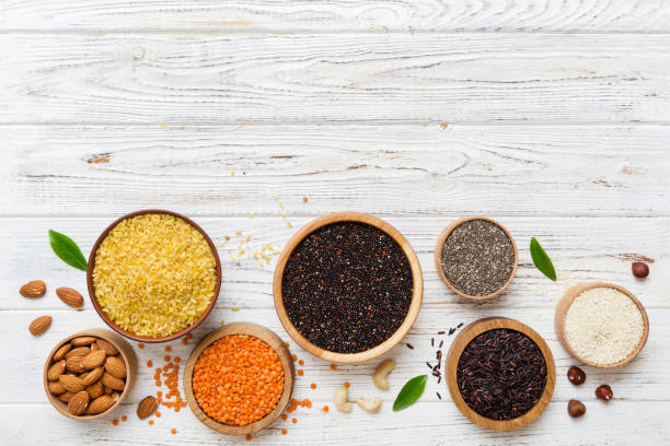 varios superalimentos en tazón pequeño sobre fondo de color. superalimentos como arroz, chía, quinoa, lentejas, nueces, semillas de sésamo, almendras. espacio de copia de vista superior - quinoa sesame chia flax seed fotografías e imágenes de stock