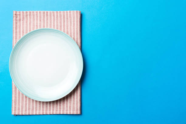 istock Top view on colored background empty round blue plate on tablecloth for food. Empty dish on napkin with space for your design 1738513804