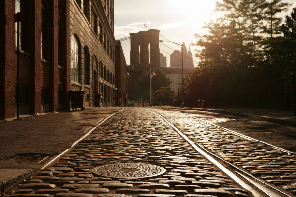 Deserted Brooklyn DUMBO Cobblestone Backstreet Sunset Lens Flare Backstreet view as the sun sets behind the Brooklyn Bridge.  Near focus on manhole cover. dumbo new york photos stock pictures, royalty-free photos & images