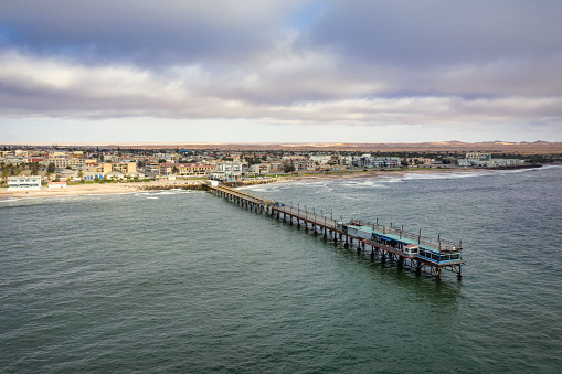 Namibia Swakopmund. Aerial Drone View of the famous Swakopmund Jetty Bridge - Pier of Swakopmund over the South Atlantic Ocean. Swakopmund Coast Beach under moody summer sky. Aerial Drone Point of View, South Atlantic Ocean, Swakopmund, Erongo Region, Namibia, Africa.