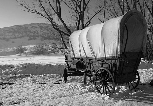 A covered wagon prairie schooner rests by a creek bed after a fresh snow fall.