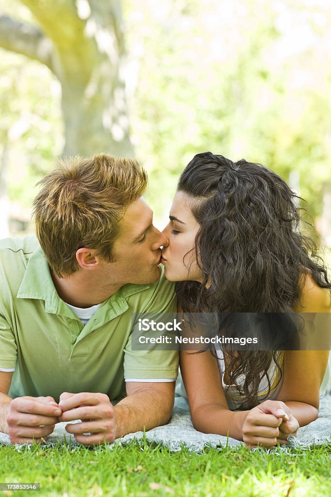 Primo piano del giovane coppia Baciare a vicenda in un parco - Foto stock royalty-free di Abbigliamento casual