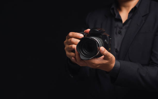 Photographer in a suit holding the digital camera while standing on a black background