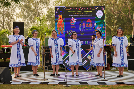 New Delhi, India - 10.12.2022 - Outdoor public park. Female choir musical ensemble of russian folk songs perform vocal music at indian charity christmas fair, group of woman singing russian folk song at outdoor stage