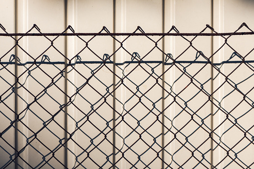 Chain link fence casting shadow on white wall as abstract background