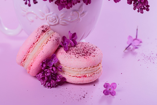 Close up of Pastel colored sweet french macaroons with lilac flowers on pink background. Beautiful composition for bakery and pastry shop
