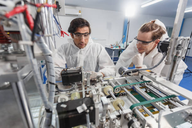 istock Team maintenance worker, face mask production machine. Male engineer wearing protective suit Inspecting quality of masks. Machine production manufacturing factory. 1738620063