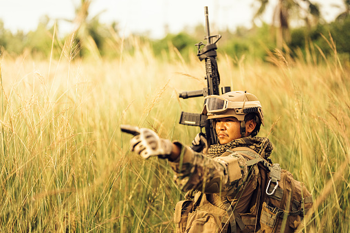 An Asian American soldier is attacking the battlefield. Point towards your goal and look ahead. There is field equipment wearing camouflage. Carrying a rifle ready to fight with enemies
