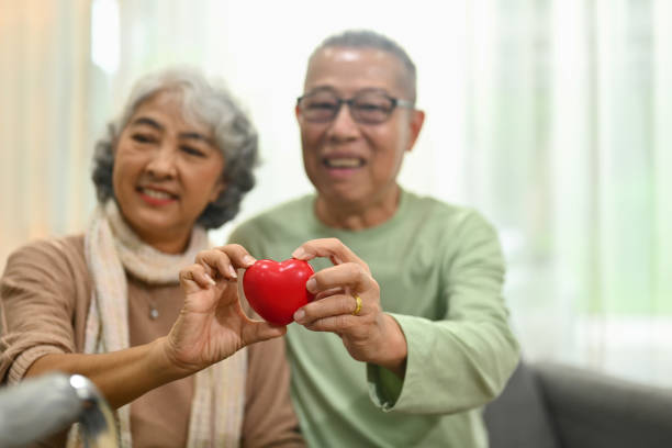 coppia anziana positiva che tiene una forma di cuore rosso come simbolo di assistenza sanitaria, amore e assicurazione - human heart care heart shape stethoscope foto e immagini stock