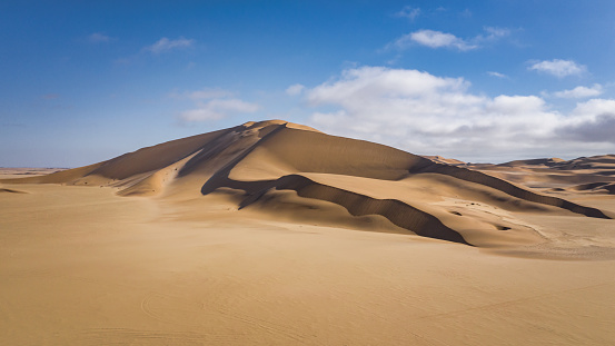 Namibia Walvis Bay - Langstrand Desert Sand Dunes. Giant Namib Desert Sand Dunes under blue summer sky. Aerial Drone Flight View towards gigantic Walvis Bay - Langstrand Sand Dunes - Namib Desert Dunes between Swakopmund and Walvis Bay, Erongo Region, Namibia, Africa