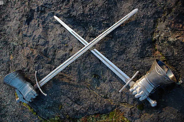 two swords and metal gloves arranged in a crossing position in front of a rock