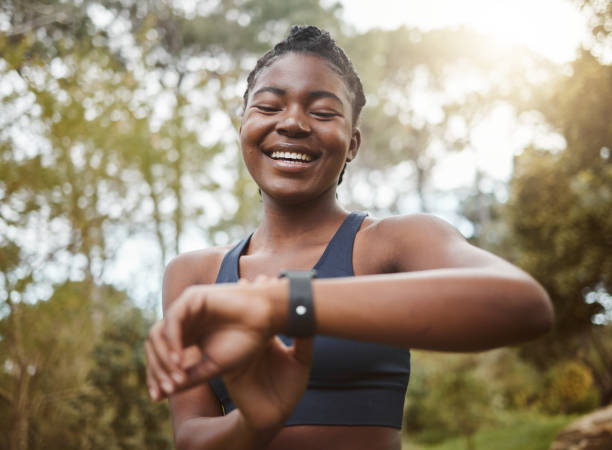 African runner woman, smart watch and park for check, smile or happy for time, results or fitness in nature. Girl, iot clock and monitor for speed, heart rate or smile for exercise, workout or health mujer corredora africana, reloj inteligente y parque para comprobar, sonreír o feliz por el tiempo, los resultados o la forma física en la naturaleza. niña, reloj iot y monitor de velocidad, frecuencia cardíaca o sonrisa para ejercicio, entrenamiento o