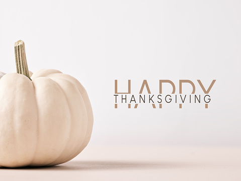 Happy Thanksgiving message with white colored Autumn pumpkin on wooden table against white background. Greeting card template.