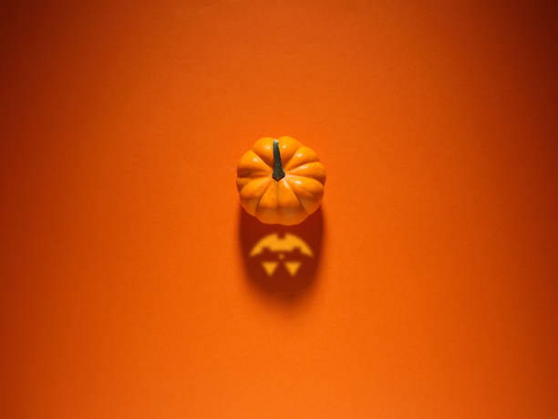 Halloween concept. Pumpkin with spooky Jack O lantern face shadow over orange colored background.
