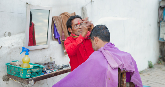 Indian barber shop - hairdresser cutting man's hair on streets of Jaipur city.
