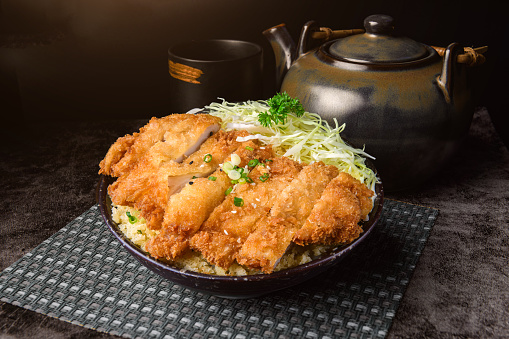Crispy Katsu chicken with sauce, rice and cabbage with dark background.