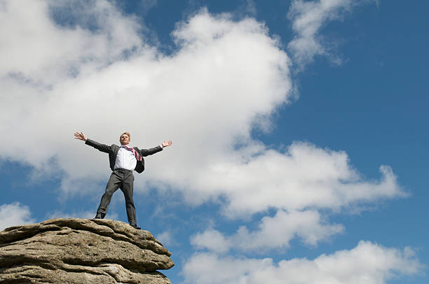 empresário de pé no topo da rocha braços spead de céu azul - people strength leadership remote imagens e fotografias de stock