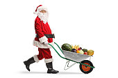 Santa claus walking and pushing a wheelbarrow with fruits and vegetables