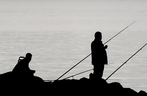 The Fascinating Silhouette of Amateur Fishermen on the Rocks Against the Sky. Nature. Seaside.Morning time.