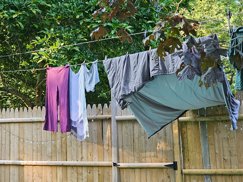 A line full of laundry over a lawn and near a fence that is bunched up.