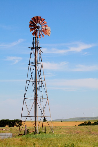 Old windmill  with modern windmills or wind turbines in the background as well as an Oklahoma wheat field.