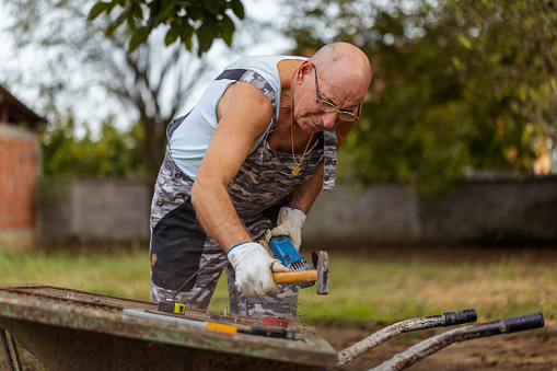 A senior artisan creating metal artistry with a hammer in his outdoor workshop.
