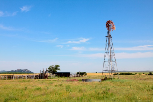 Old windmill and corral with modern windmills or turbines in the background as well as an Oklahoma wheat field and blue sky. Agriculture image.