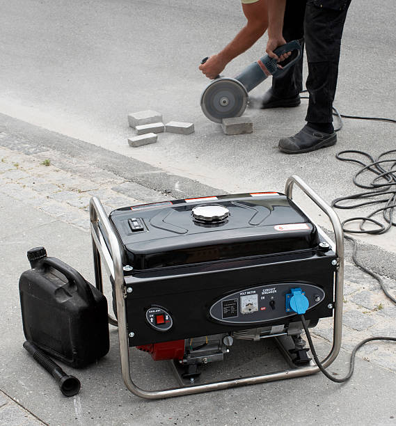 Electrical generator in foreground and man using masonry saw stock photo