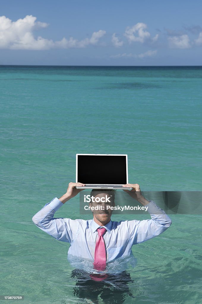 Sorridente Uomo d'affari tiene un portatile sulla testa in mare - Foto stock royalty-free di Abbigliamento elegante