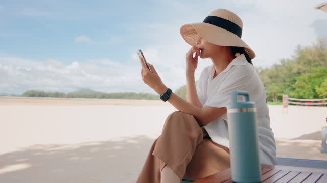 Beach side Connection: Woman in Beach wearing Hat Enjoys Mobile Phone by the Sea
