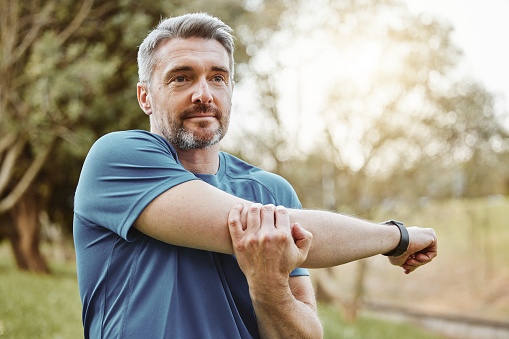 Mature man, arm stretching and outdoor for fitness, wellness and exercise in a park for health. Morning, athlete and training in nature with workout and sports of a calm person ready to start run