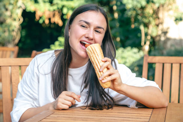 istock A young woman eats a hot dog on a cafe terrace. 1738744230