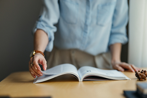 An unrecognizable Caucasian student standing at the desk and reading a book.