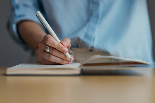 A close up view of an unrecognizable Caucasian student using her pen and a notebook while studying.