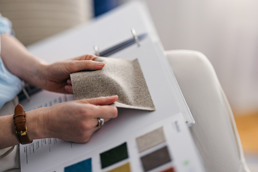 A cropped view of an unrecognizable Caucasian interior designer looking at various carpet samples while sitting in the living room. (close up)