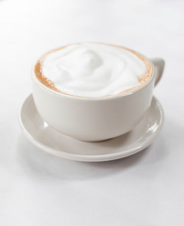 A coffee cup with a coffee drink and foamed milk on top.