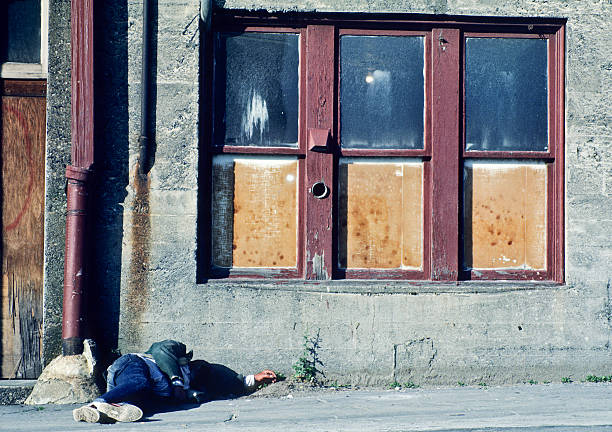 London, United Kingdom - May 29, 2011: Middle aged man leaning against a wall sleeping in Covent Garden.  His head rests in his hand as he leans against a cement wall, sound asleep while street performers entertain crowds a few feet away.