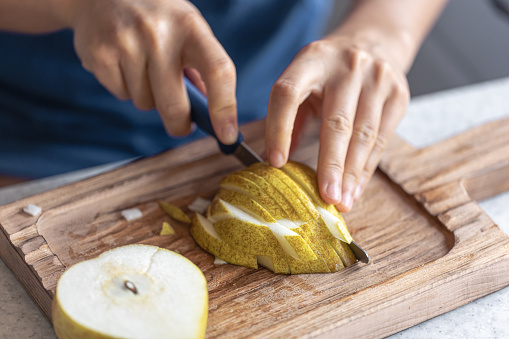 A woman cuts a pear into small pieces on a wooden cutting board, close-up.