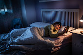 Teenage girl suffering insomnia checking time in smartphone at night