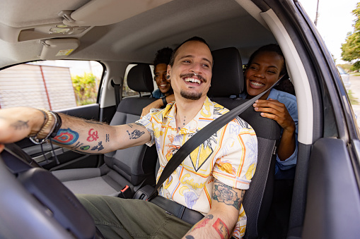 Happy driver enjoying while driving his African American customers in a car.