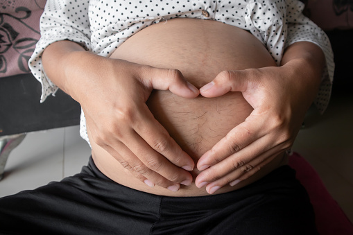 A pregnant woman makes a heart shape with her hands on her stomach.