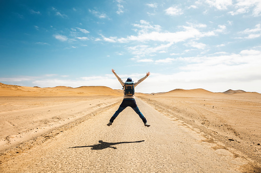 Excited young traveler man jumping on desert road. Freedom and success concept.