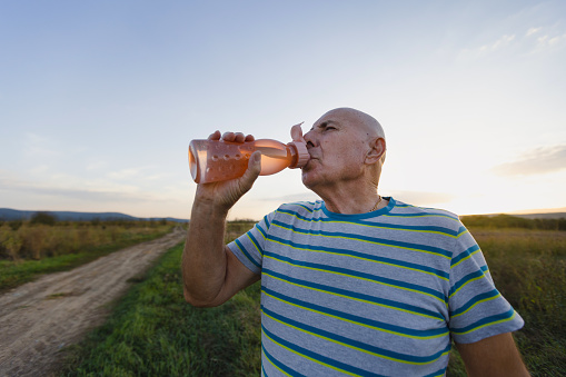 A serene image of a senior man, taking a refreshing sip from his water bottle, immediately after a revitalizing walk in the natural wilderness.