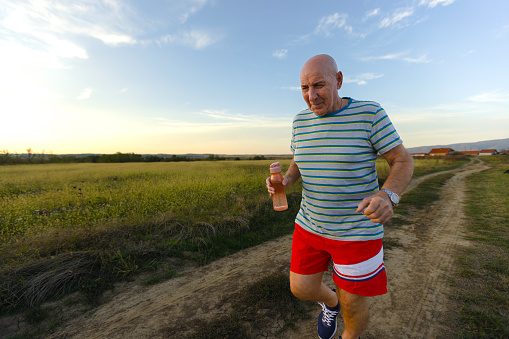 An active senior man in sports attire jogging amidst a breathtaking natural landscape as the sun sets.