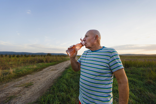 A senior man enjoys a refreshing sip of water from a bottle, reinvigorated by his nature walk.