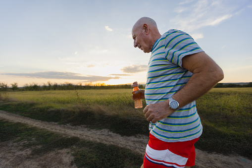 A senior gentleman donning sportswear gracefully sprints through the serene beauty of nature during a stunning sunset.